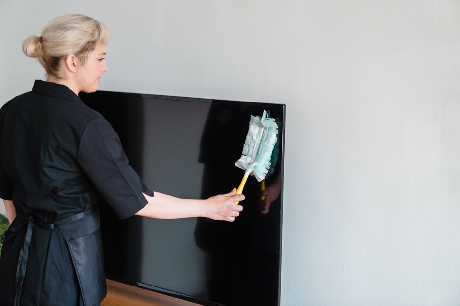 A professional cleaner from Crystal Palace Cleaners is using a blue cloth to wipe a surface, possibly a countertop or window sill, in a well-lit room with large white curtains allowing natural light t